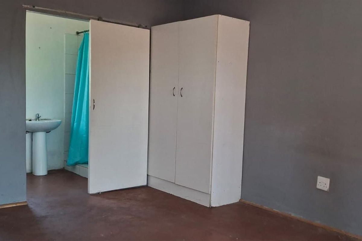 A bedroom featuring a built-in wardrobe and an en-suite bathroom with a pedestal basin and shower area.