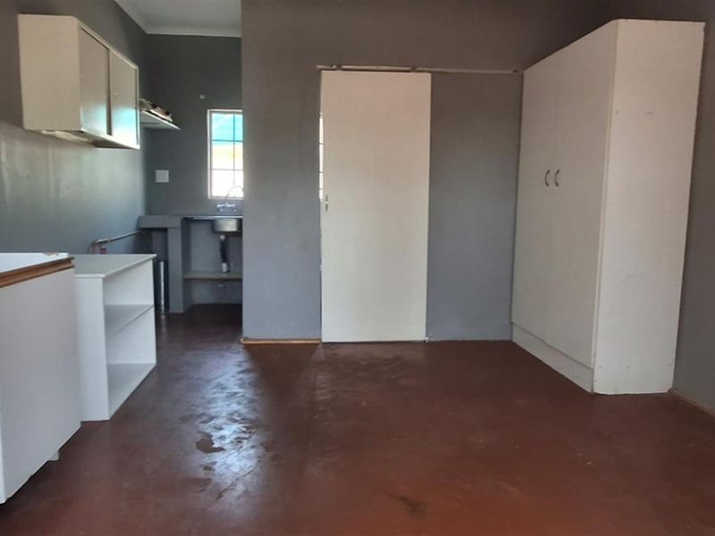 A basic, empty kitchen area featuring built-in cabinetry, a sink, and a built-in cupboard, with painted walls and a concrete floor.