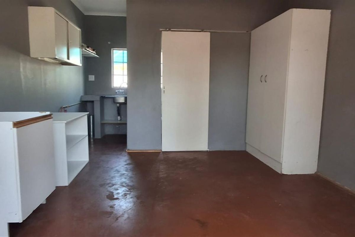 A basic, empty kitchen area featuring built-in cabinetry, a sink, and a built-in cupboard, with painted walls and a concrete floor.