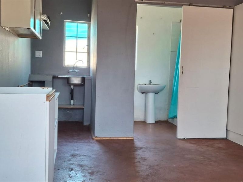 Open plan studio space featuring a basic kitchenette with sink, adjacent bathroom with pedestal basin, and built-in storage cupboards.