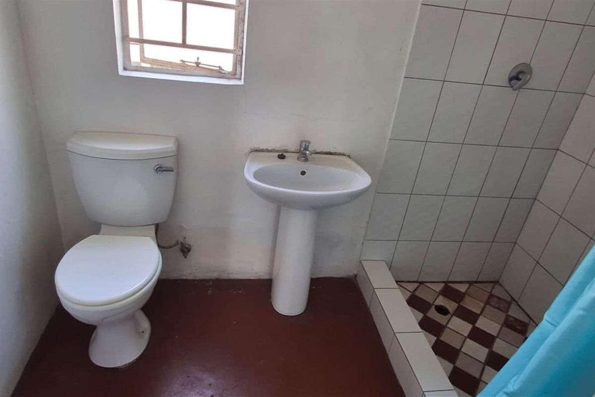 A functional bathroom featuring a pedestal basin, toilet, and a tiled shower enclosure with a window providing natural light.