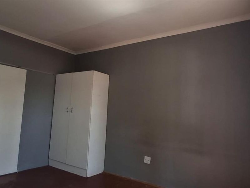 A simple, empty bedroom featuring dark grey walls, a built-in wardrobe, and a large steel-framed window allowing natural light.