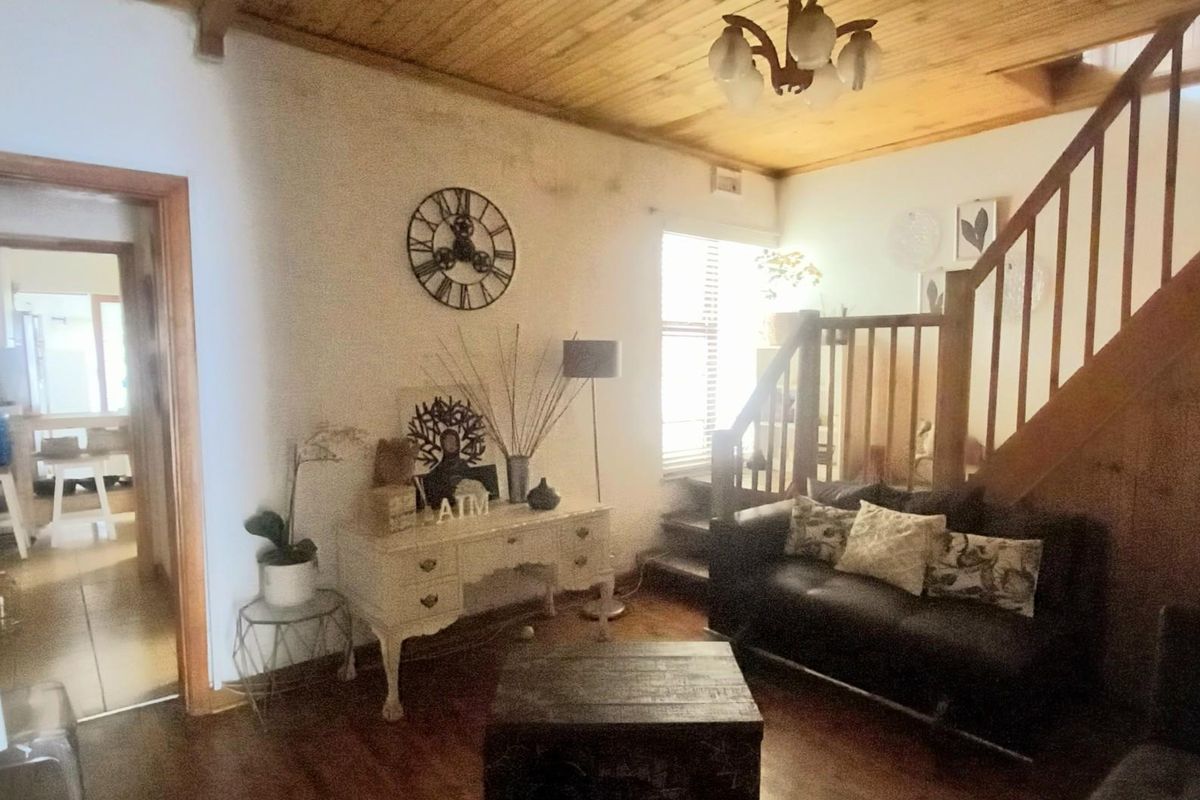 Living room featuring timber ceiling, timber staircase with balustrade, and timber flooring, showing signs of wear and wall staining.