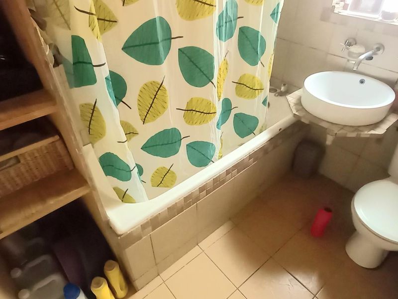 A compact bathroom featuring a bathtub with shower curtain, wall-mounted basin, and toilet, finished with tiled walls and flooring.