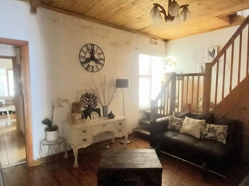 Living room featuring timber ceiling, timber staircase with balustrade, and timber flooring, showing signs of wear and wall staining.