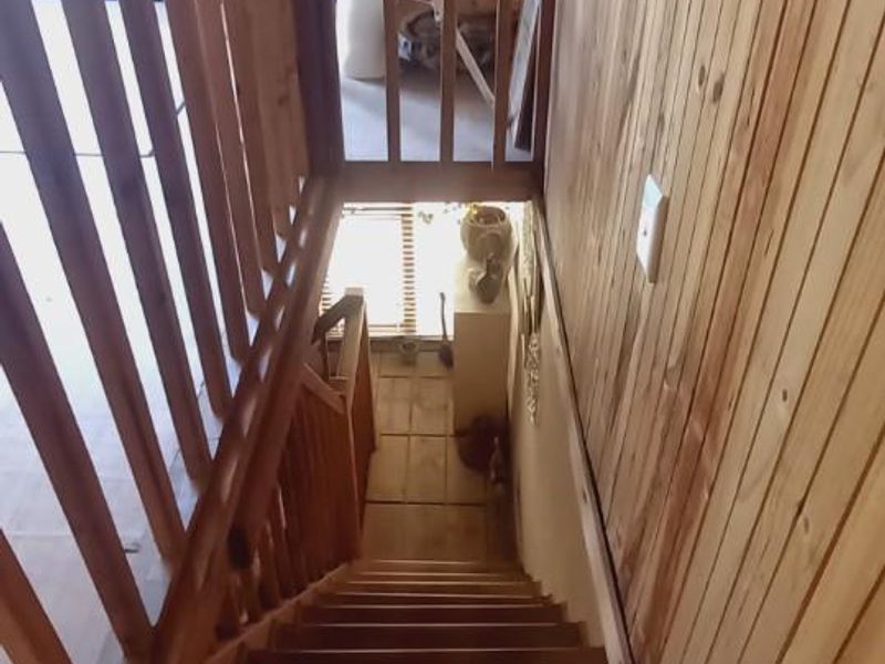 A narrow staircase featuring timber wall cladding and a wooden balustrade, showing signs of wear and dated finishes.