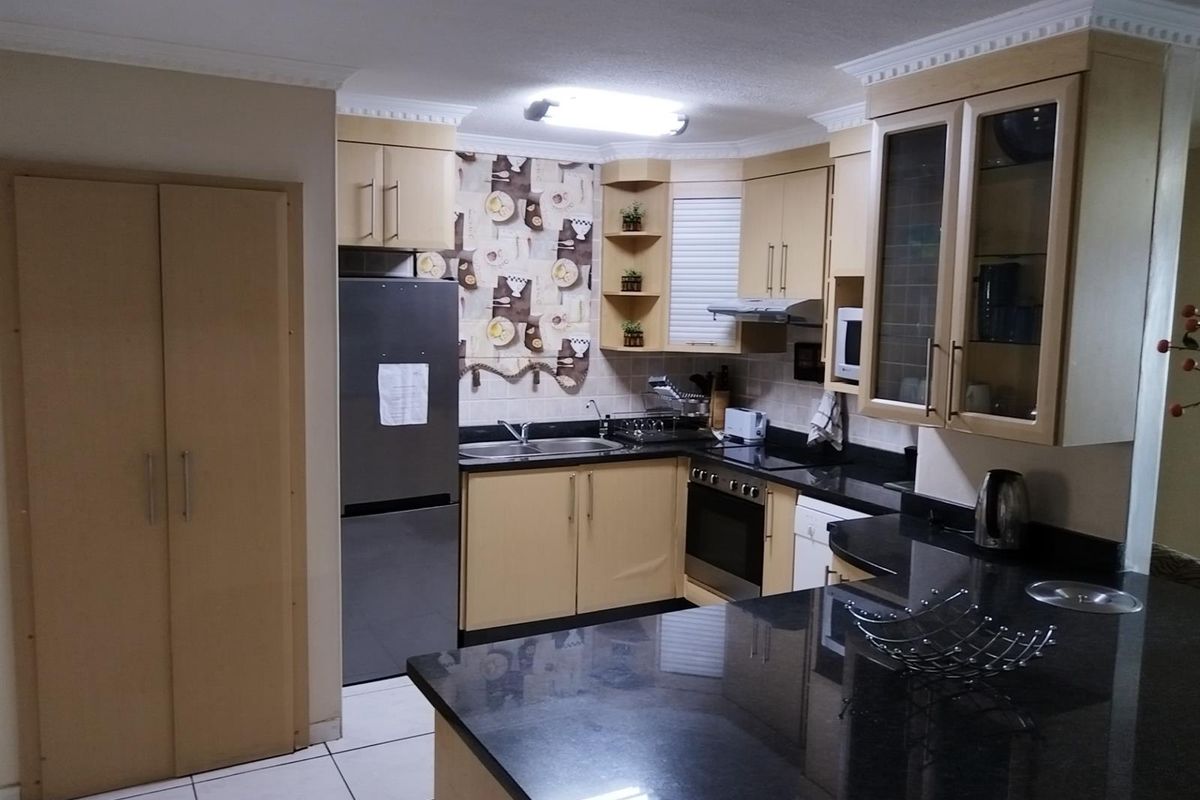 A functional kitchen featuring light wood cabinetry, dark granite countertops, a built-in oven, and a double sink with tiled flooring.