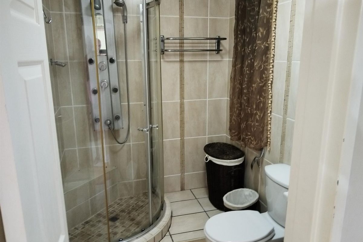 A compact bathroom featuring a curved glass shower enclosure with a built-in massage panel, tiled walls, and a standard toilet.
