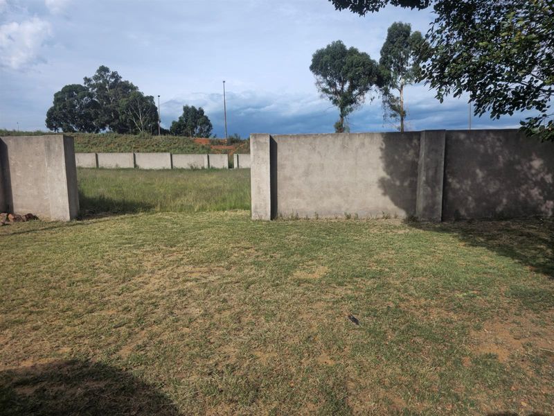 A vacant residential plot featuring established perimeter concrete boundary walls and open grassed terrain, suitable for future development.