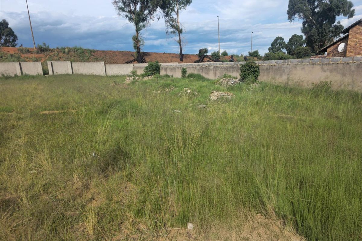 A vacant residential plot featuring perimeter boundary walls and overgrown grass, offering a blank canvas for future development.