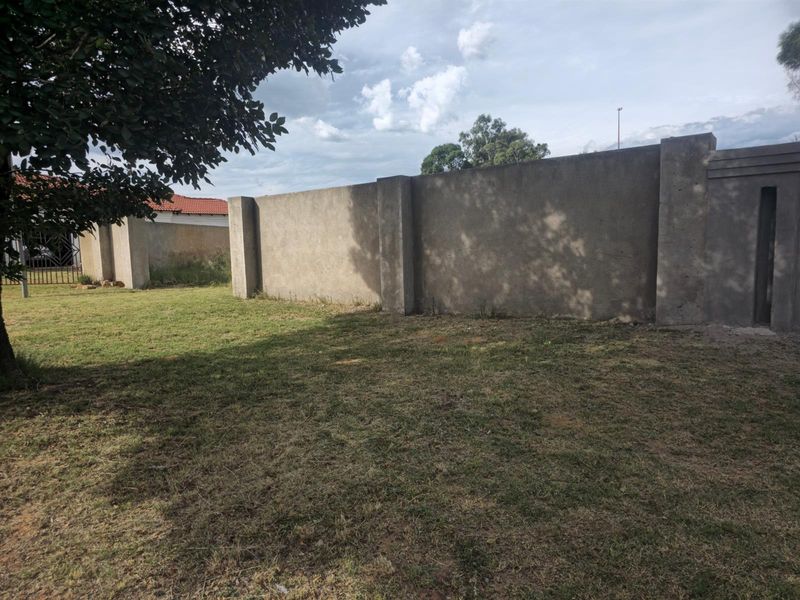 A view of a residential vacant land plot featuring a perimeter concrete boundary wall and established lawn area.