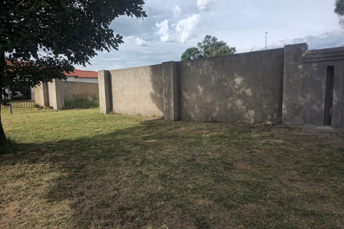 A view of a residential vacant land plot featuring a perimeter concrete boundary wall and established lawn area.