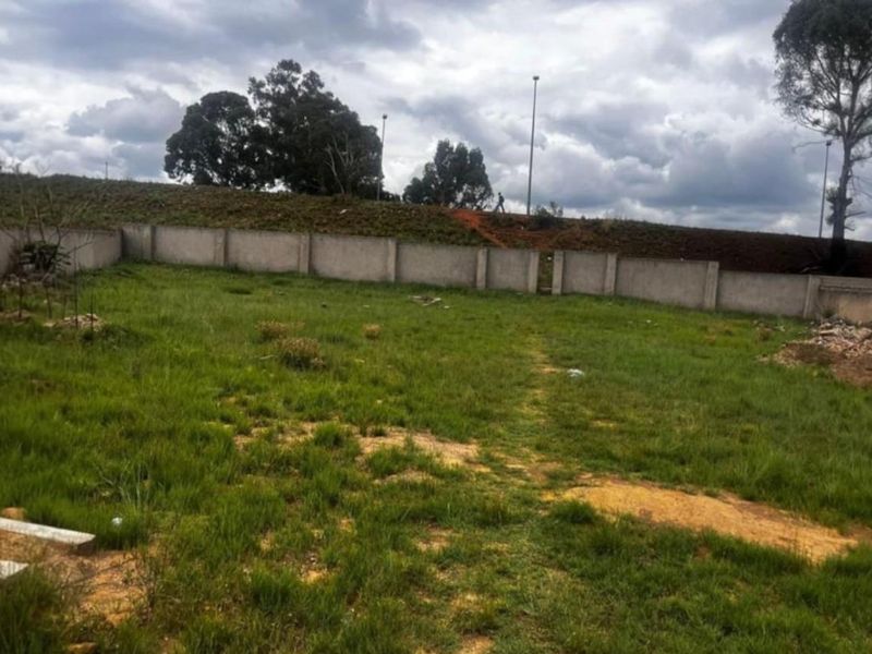 A vacant residential plot featuring a perimeter concrete boundary wall and established grass coverage, ready for development.