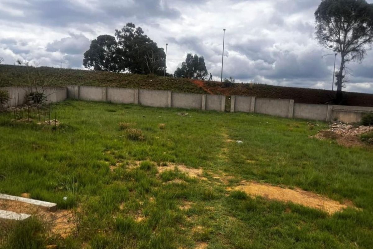 A vacant residential plot featuring a perimeter concrete boundary wall and established grass coverage, ready for development.