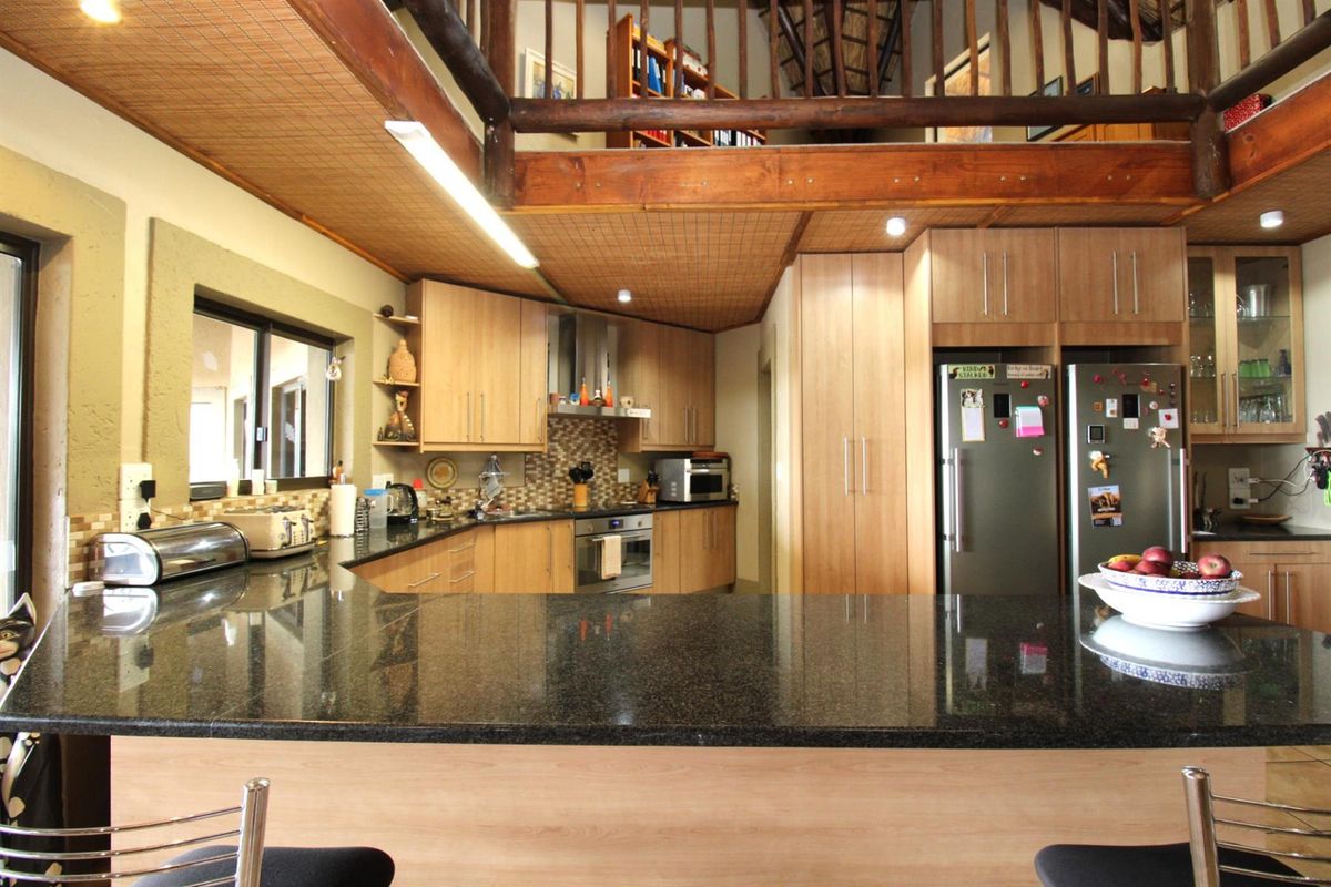 A well-appointed kitchen featuring granite countertops, light wood cabinetry, a built-in oven, and a breakfast bar, with an open mezzanine level above.