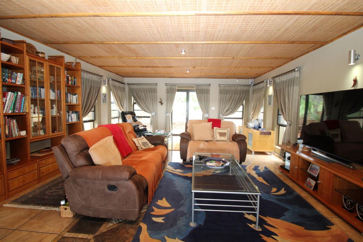 Spacious living room featuring a unique bamboo-style paneled ceiling, tiled flooring, and large windows providing natural light and garden access.