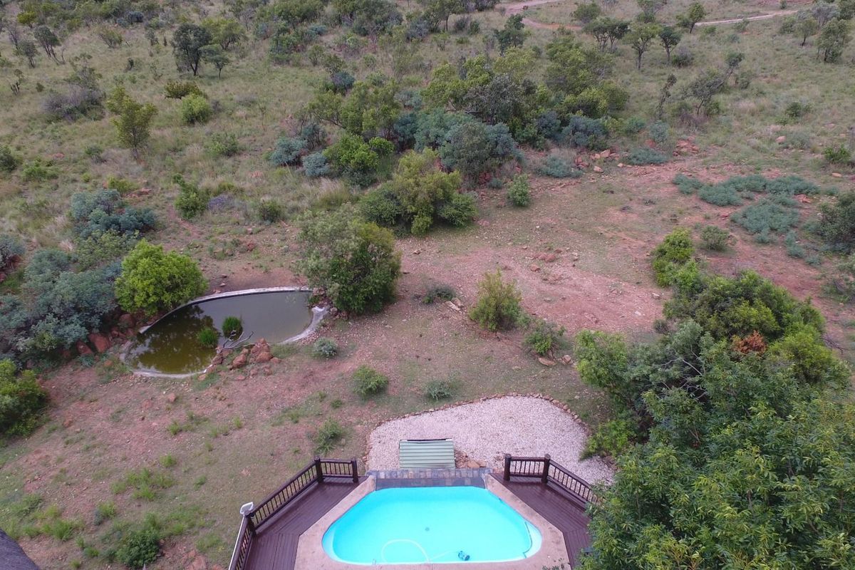 Aerial view of a swimming pool with a wooden deck, overlooking a natural landscape with a small pond.