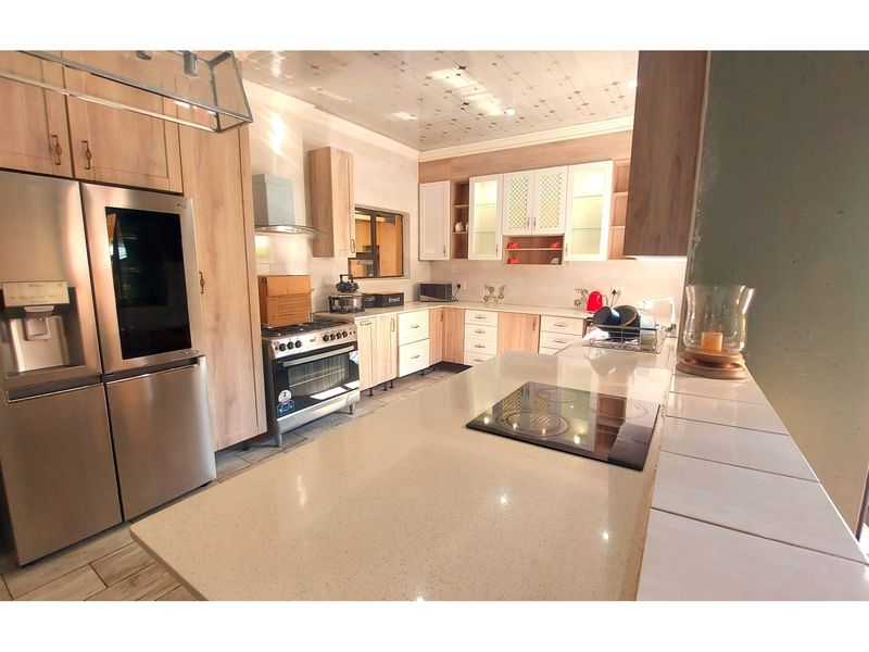 A functional kitchen featuring light wood cabinetry, stone countertops, a central island with an integrated hob, and a tiled ceiling finish.