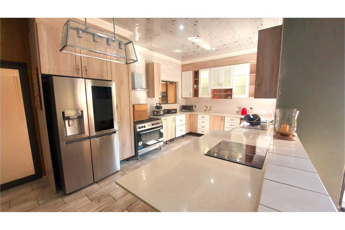 Modern kitchen featuring light wood cabinetry, stone countertops, a central island with a built-in cooktop, and high-quality tiled flooring.