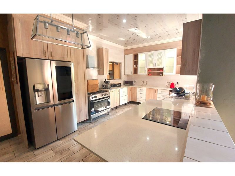 Modern kitchen featuring light wood cabinetry, stone countertops, a central island with a built-in cooktop, and high-quality tiled flooring.