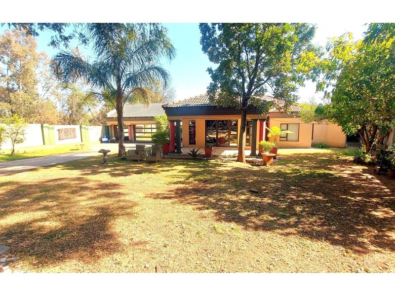 Spacious rear garden featuring a covered patio with decorative columns, paved driveway, and established trees, offering a private outdoor living space.