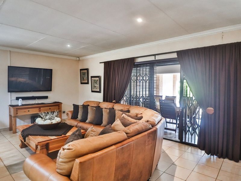 Spacious living room featuring tiled flooring, recessed lighting, and large sliding glass doors with security gates providing access to the outdoor patio area.