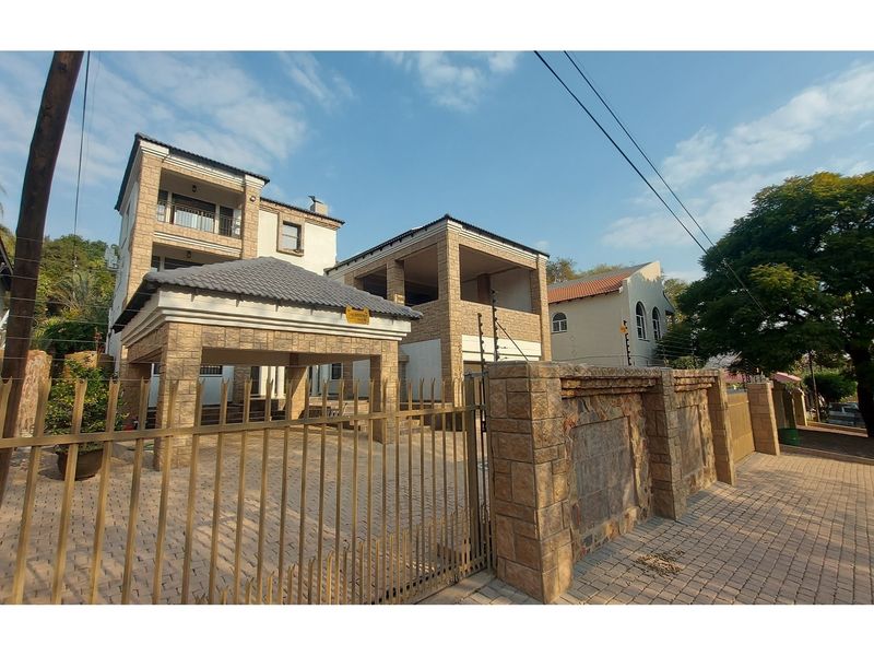 Front elevation of a multi-story residential property featuring stone cladding, a paved driveway, and secure perimeter fencing with an unfinished construction section.