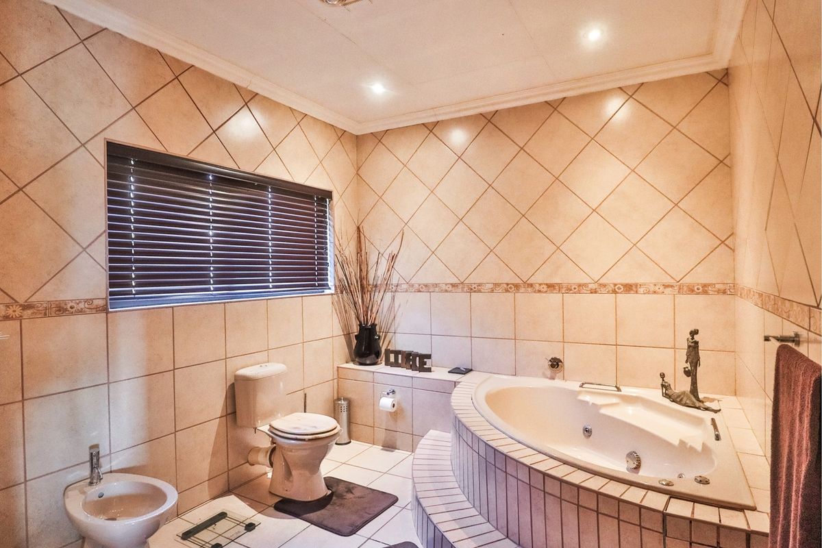 A spacious bathroom featuring a built-in corner bathtub, a toilet, and a bidet, finished with neutral wall and floor tiling.