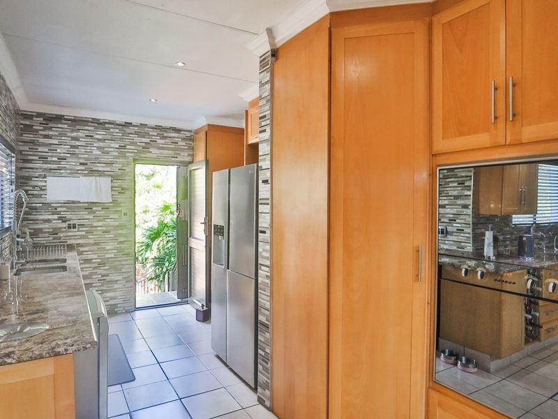 A functional kitchen featuring warm wood cabinetry, stone countertops, mosaic tile backsplash, and integrated oven, with direct access to an outdoor area.