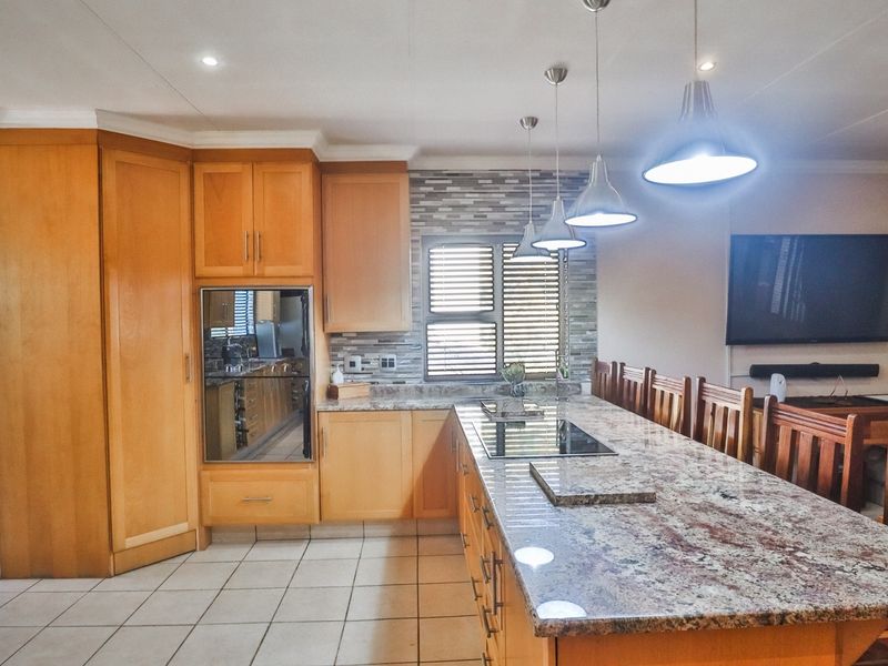 Spacious kitchen featuring wooden cabinetry, granite countertops, a built-in oven, and a central island with an integrated hob, perfect for cooking and casual dining.