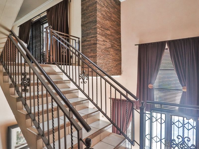 An elegant entrance hall featuring a tiled staircase with decorative wrought iron balustrades and a striking stone feature wall.