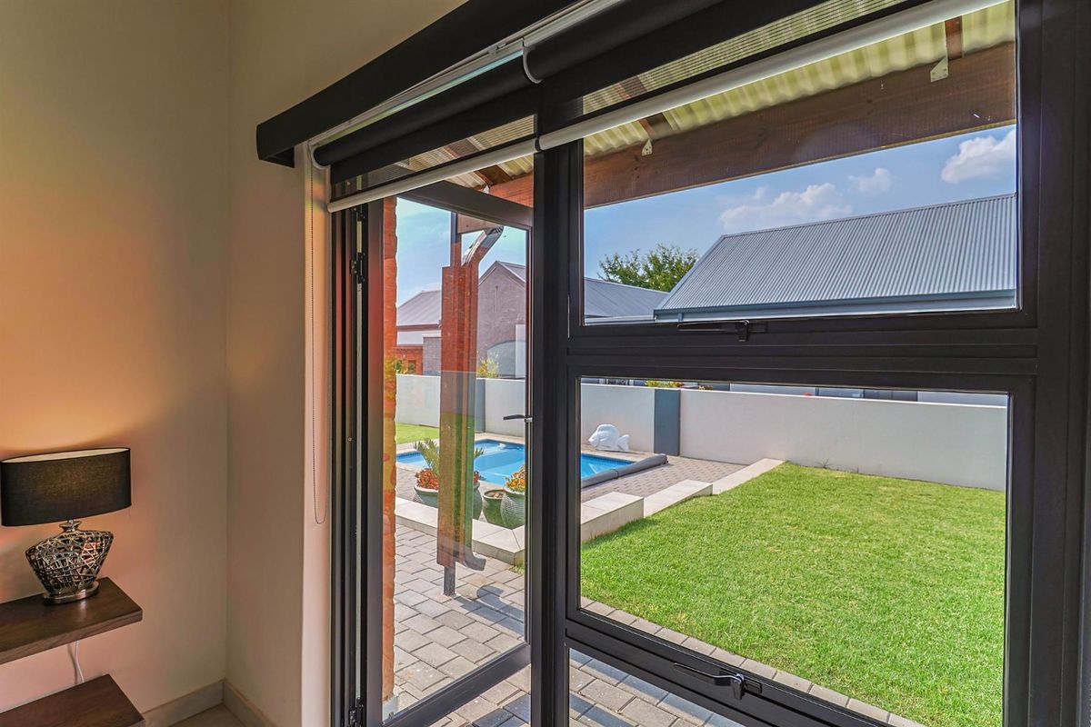 View from an interior space looking out through modern black-framed glass doors towards a private garden with a swimming pool and paved patio area.