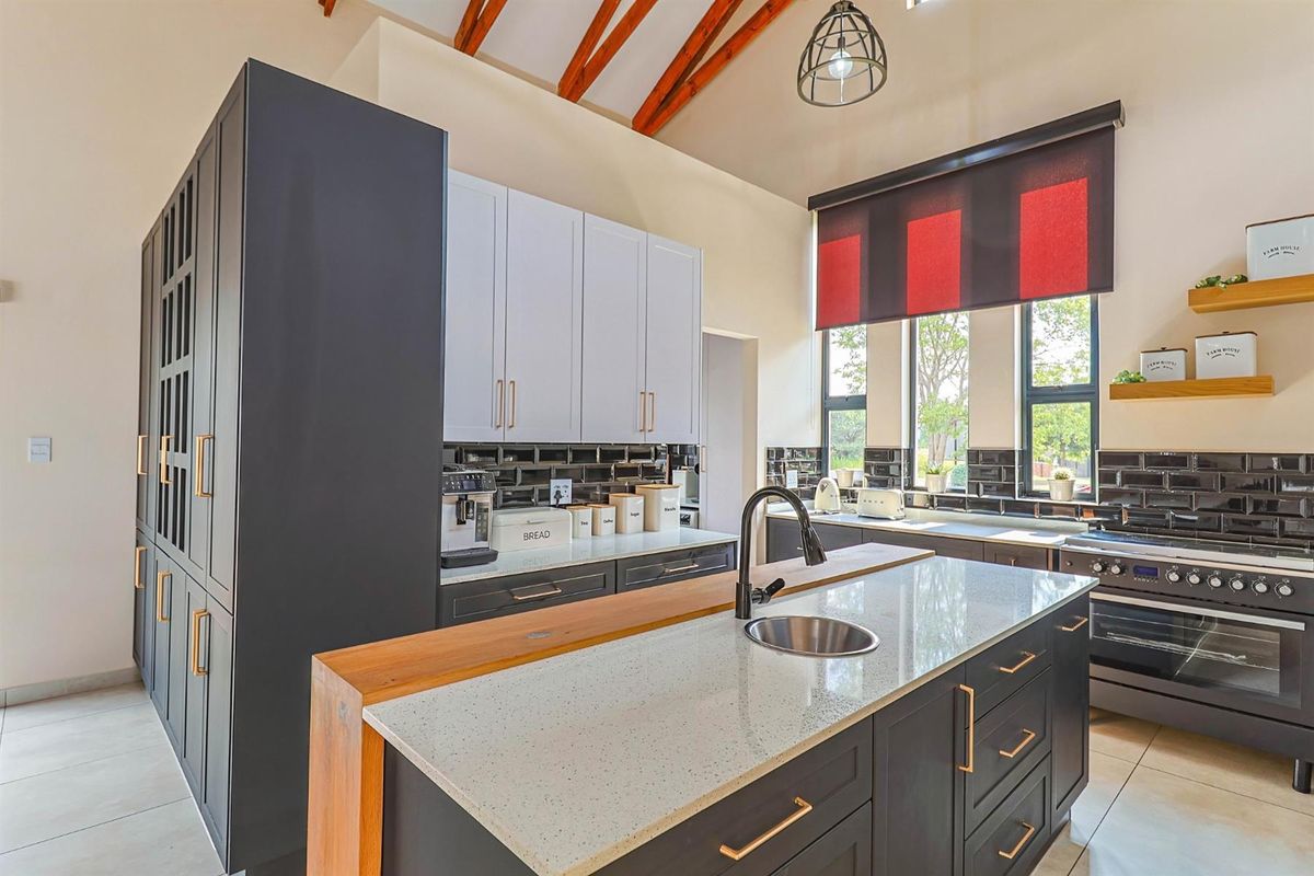 Modern kitchen featuring a central island with stone countertop, dark cabinetry, subway tile backsplash, and high vaulted ceilings with exposed timber beams.