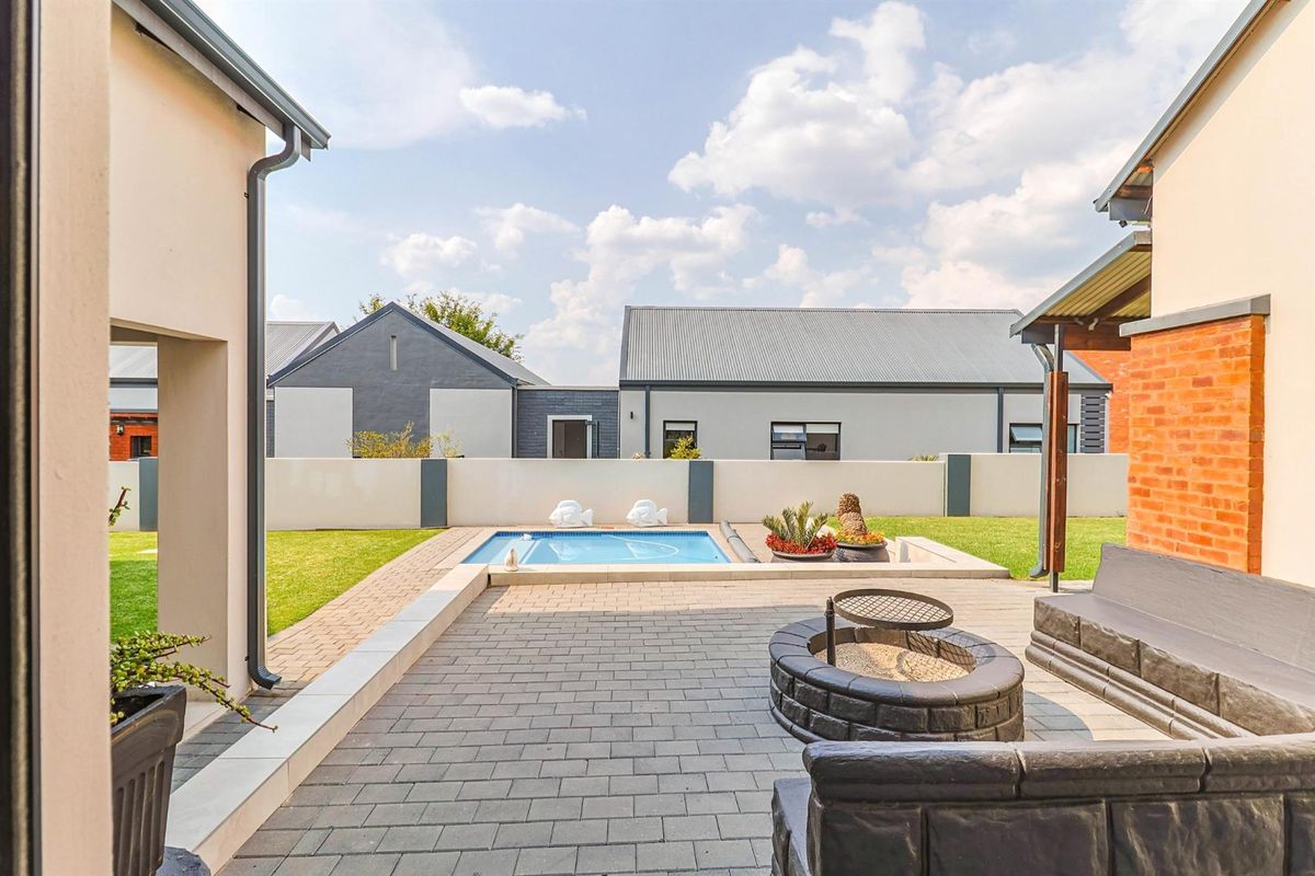 A well-maintained rear garden featuring a paved patio area, a built-in fire pit, and a swimming pool set within a landscaped lawn.