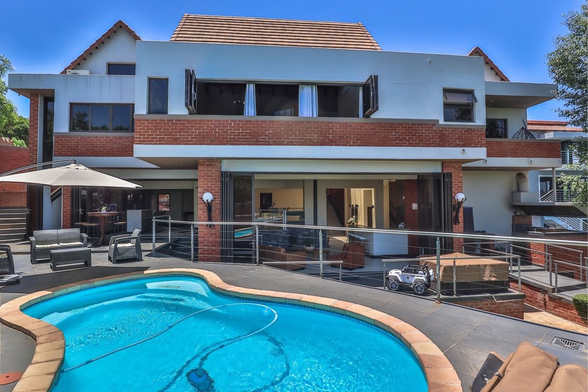 Rear view of the property featuring a swimming pool, spacious tiled patio area, and large bi-fold doors leading into the open-plan living space.