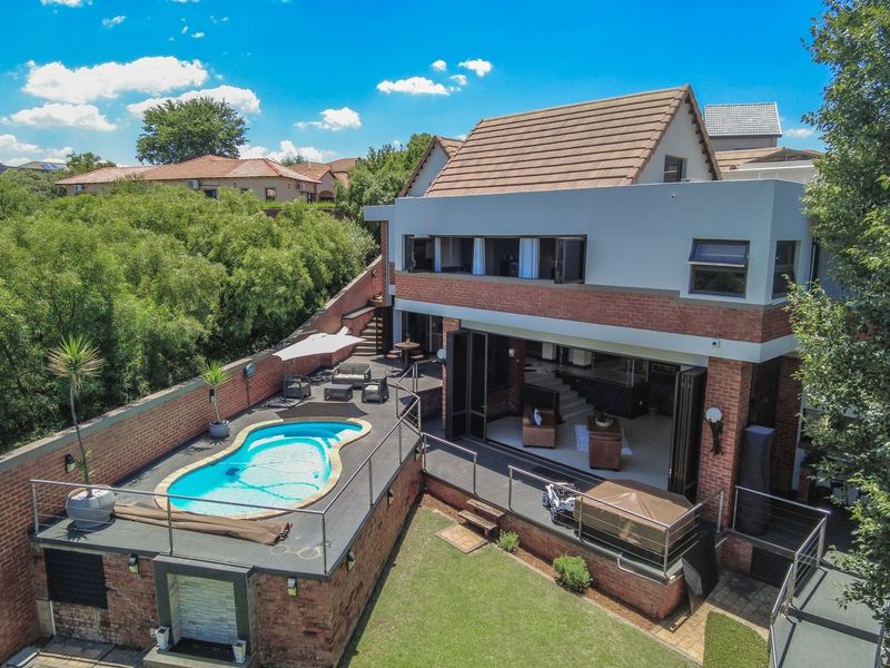 Aerial view of a multi-level residential property featuring a swimming pool, spacious patio area, and brick exterior with large folding glass doors.