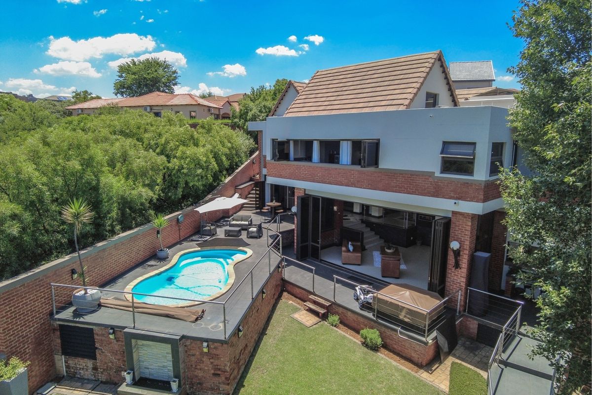 Aerial view of a multi-level residential property featuring a swimming pool, spacious patio area, and brick exterior with large folding glass doors.