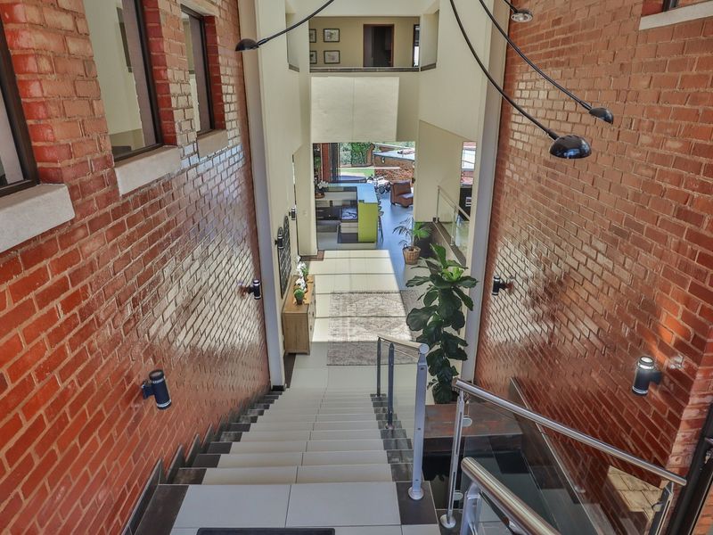 A striking double-volume entrance hallway featuring exposed brick walls, a tiled staircase with modern glass balustrades, and views through to the living area.