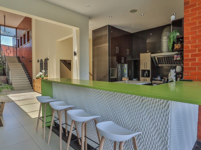 Spacious open-plan kitchen featuring a modern breakfast bar, sleek cabinetry, and an exposed brick feature wall, seamlessly connecting to the main staircase area.