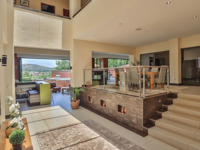 Spacious open-plan living area featuring a raised dining platform with glass balustrades, tiled flooring, recessed lighting, and seamless access to an outdoor patio.