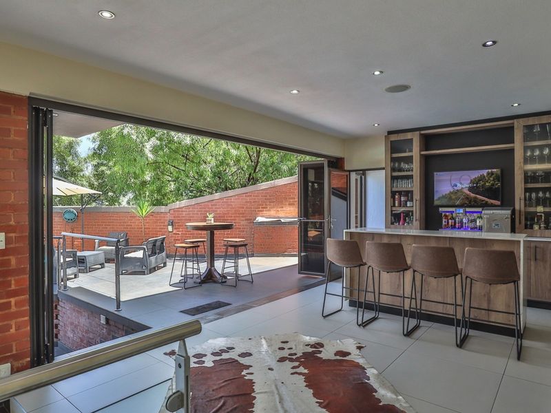 Modern indoor bar area featuring built-in cabinetry and counter, seamlessly opening to an outdoor patio through large bi-fold doors.