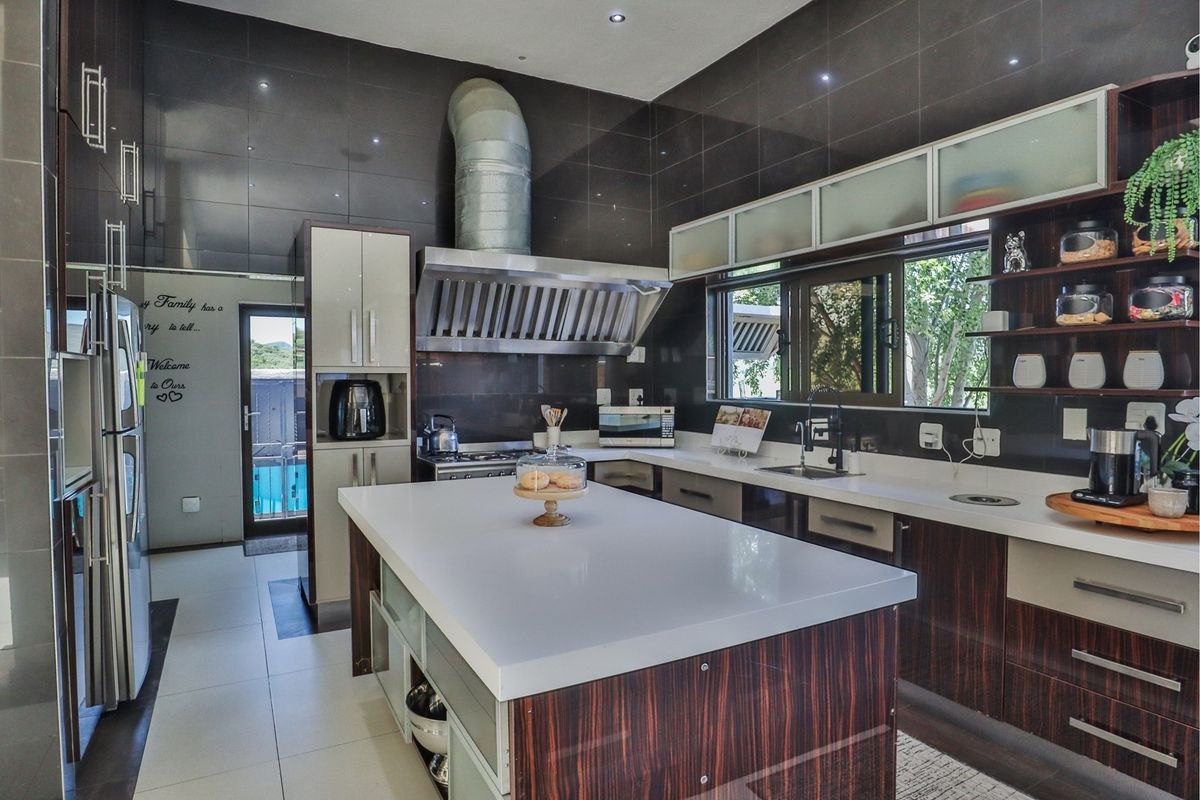 Modern kitchen featuring a large central island, stone countertops, dark tiled walls, and high-quality stainless steel appliances including a prominent extractor fan.