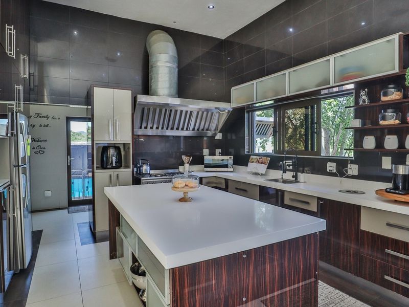 Modern kitchen featuring a large central island, stone countertops, dark tiled walls, and high-quality stainless steel appliances including a prominent extractor fan.