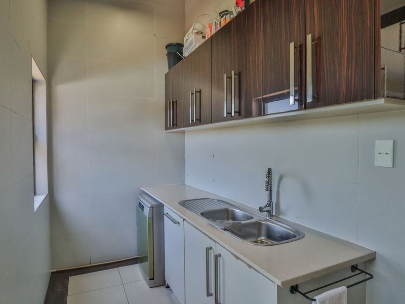 A functional scullery featuring dark wood upper cabinetry, white lower cabinets, a stainless steel double sink, and tiled finishes throughout.