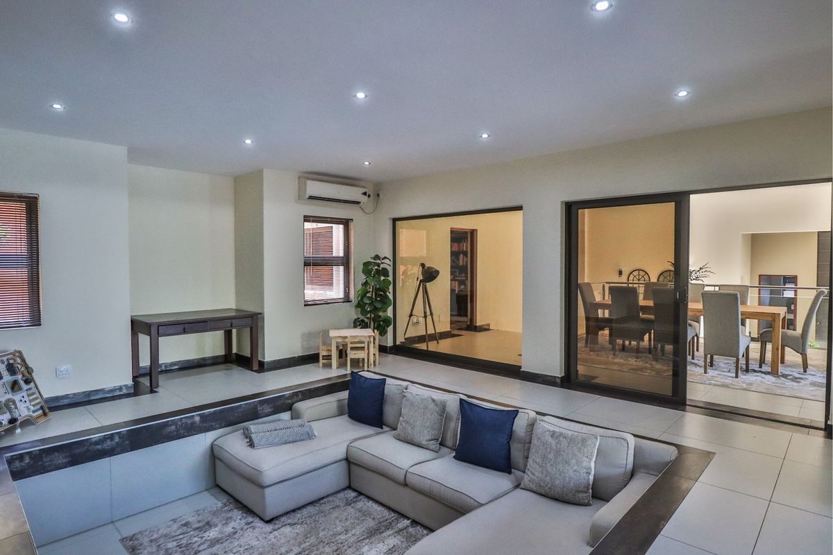 Spacious sunken living room featuring tiled floors, recessed downlighting, split-system air conditioning, and large glass doors providing views into the adjacent dining area.