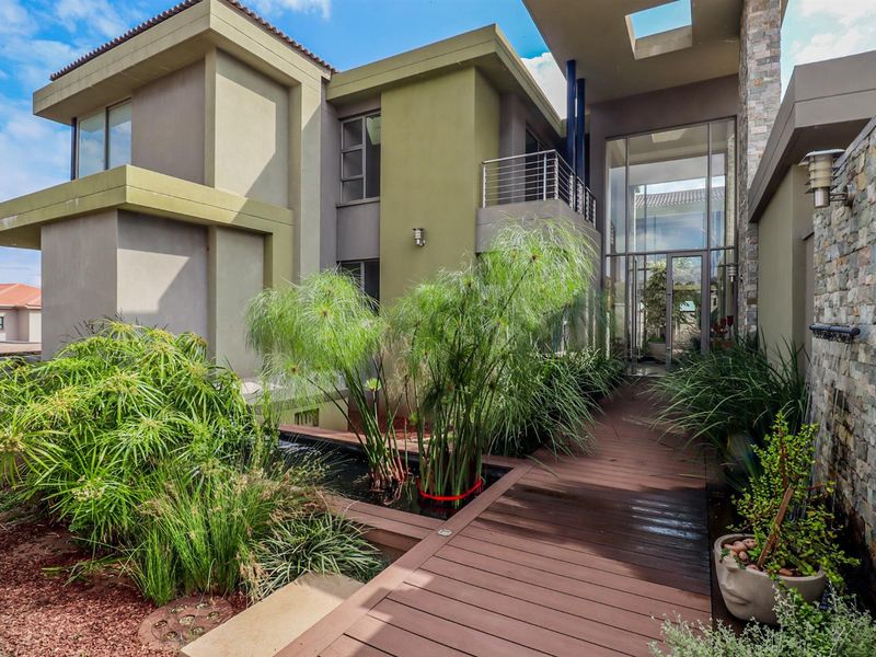 Modern architectural entrance featuring a timber walkway over a water feature, stone cladding, and expansive glass facade elements.