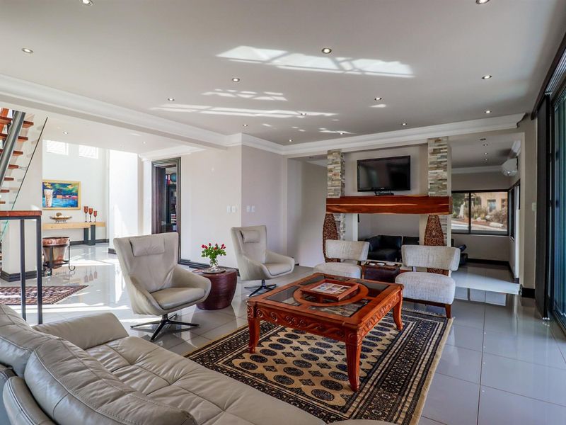 Spacious living room featuring a stone-clad fireplace, polished porcelain flooring, recessed lighting, and a modern staircase with glass balustrades.