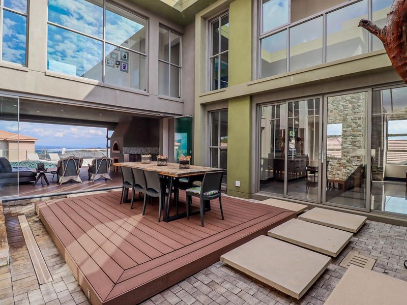 A modern, multi-level outdoor entertainment area featuring composite decking, stone accents, large sliding glass doors, and a built-in braai facility.