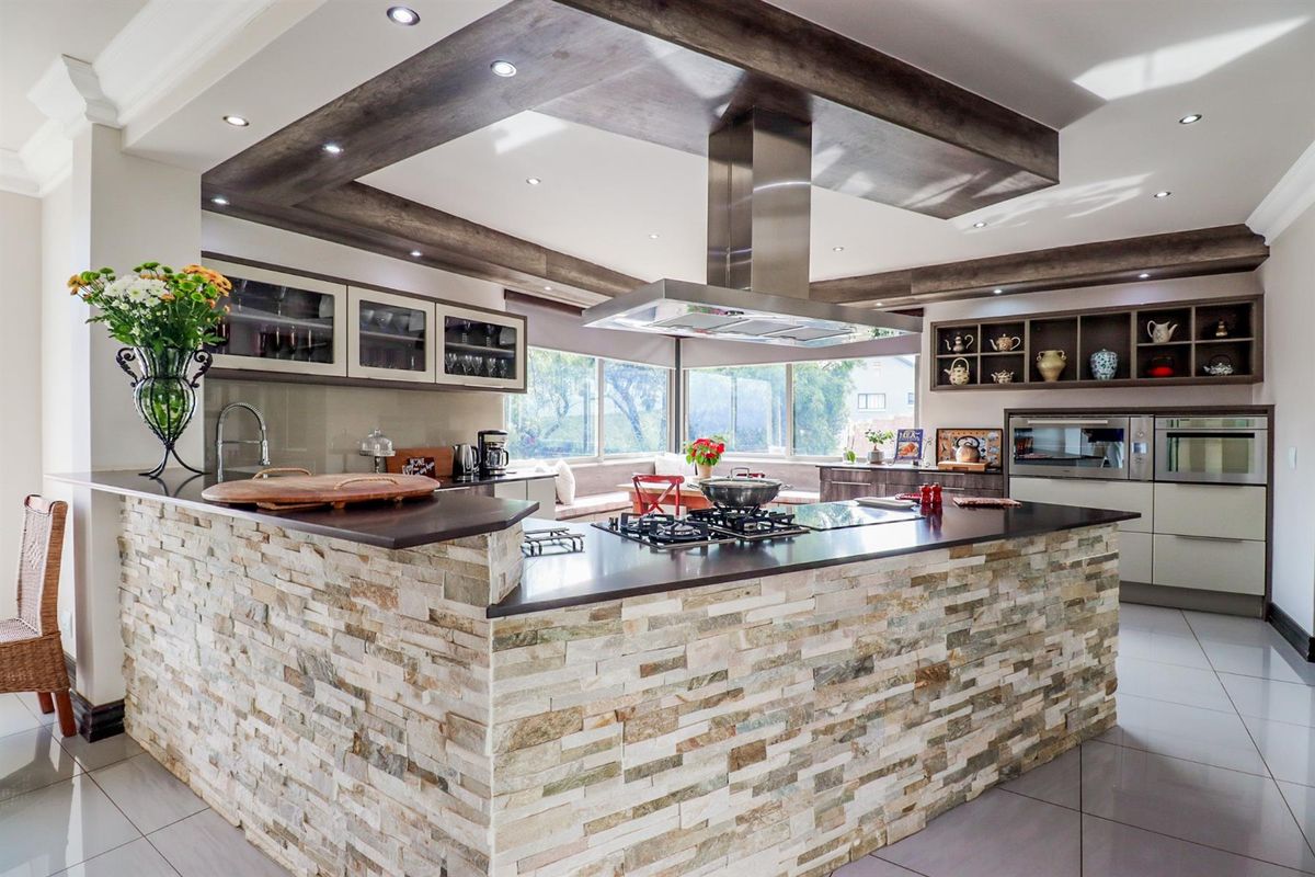 Modern kitchen featuring a stone-clad island with a gas hob, stainless steel extractor, built-in appliances, and recessed ceiling lighting.