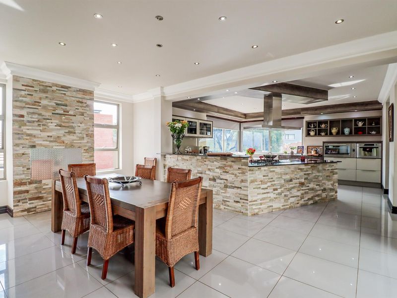 Spacious open-plan living and dining area featuring a modern kitchen with stone-clad island, built-in appliances, and polished porcelain floor tiles.